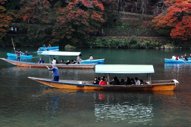 紅葉に囲まれた川に浮かぶ、屋根付きの舟と手こぎボート