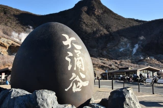 噴煙の上がる山肌と、黒たまごの形をした大涌谷の石碑