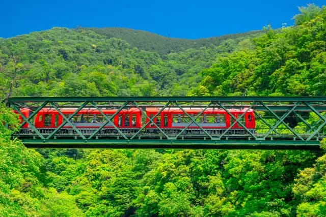 A red train crossing a truss bridge above a green valley